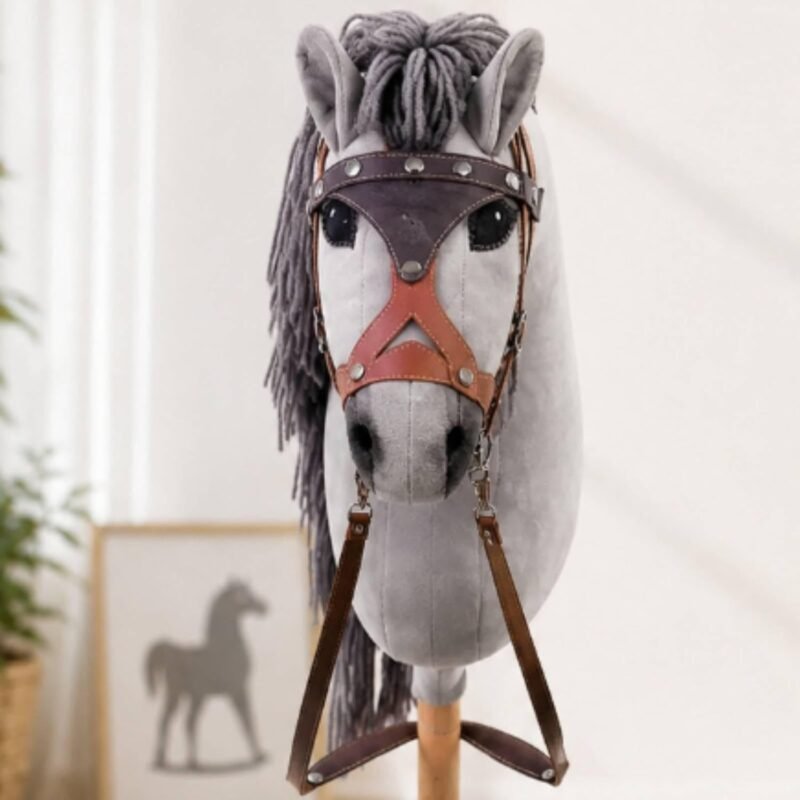 Vue de face du cheval bâton gris clair avec bride western marron et œillères dans une pièce lumineuse