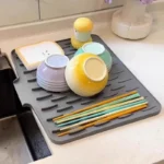 Tapis égouttoir en silicone gris près de l’évier avec bols et baguettes en train de sécher