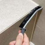 Main nettoyant un joint de carrelage étroit dans une salle de bain avec la brosse à joints fine