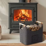 Panier à bûches en feutre gris foncé avec poignées en bois rempli de bois à côté d’un poêle