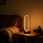 Lampe de table ovale à anneau LED diffusant une lumière chaude sur une table d’appoint à côté d’un canapé en cuir et d’un appareil photo vintage