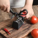 Aiguiseur de couteaux rouge et noir sur une planche en bois avec des ciseaux en cours d’affûtage