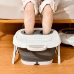 Pieds trempant dans le bain de pieds pliable sur un parquet devant un canapé